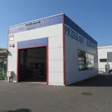 Budynek stacji kontroli pojazdów z napisem "Przeglądy Rejestracyjne" i otwartą bramą wjazdową.