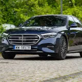 Elegancki, ciemnogranatowy Mercedes z napędem 4matic, zaparkowany na brukowanej nawierzchni, otoczony zielenią.