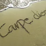 Napis "Carpe diem" na piasku, tuż przy falach. To przypomnienie o ulotnych chwilach i złotych myślach.