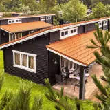 Czarny bungalow z pomarańczowym dachem, otoczony zielenią. Na werandzie stolik i krzesła.