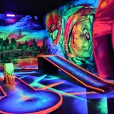 Neon-beleuchtete Bahnen und eine Skyline-Kulisse laden zum **Glow Minigolf** ein. Ein Superheld wacht über das Spiel.