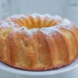 Puszysta babka wegańska, oprószona cukrem pudrem, prezentuje się apetycznie na białej paterze. Idealna na każdą okazję.
