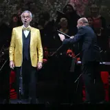 Andrea Bocelli w złotej marynarce śpiewa na scenie, dyrygent prowadzi orkiestrę. Koncert zapowiada się na niezapomniane przeżycie, jakiego można spodziewać się po Andrea Bocelli koncert 2026.