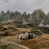 Majestätische Berge im Val di Funes, ein Hotel auf einem Hügel, umgeben von herbstlichem Gras und einer Straße.