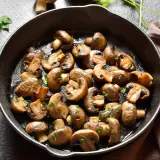 Usmażone pieczarki do obiadu, posypane natką pietruszki, w czarnej patelni.