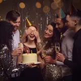 Grupa przyjaciół świętuje urodziny w domu. Jubilatka z zasłoniętymi oczami czeka na niespodziankę z tortem. To świetne, fajne atrakcje na urodziny w domu!
