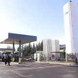 Stacja tankowania CNG. Żółte autobusy czekają pod wiatą, obok wysoki zbiornik i instalacja.
