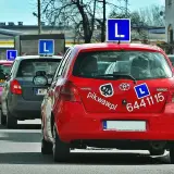 Czerwony samochód nauki jazdy z literą "L" na dachu. Zastanawiasz się, ile zarabia instruktor jazdy?