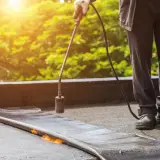 Pracownik z palnikiem gazowym uszczelnia papę na dachu. Dobór odpowiednich szpilek do murłaty jest kluczowy dla trwałości pokrycia.