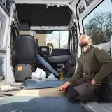 Uomo lavora all'isolamento di un'auto camperizzata. Materiali sparsi, sedili rimossi, pronto per la trasformazione.