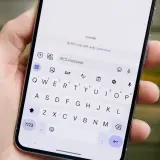 Dłoń trzyma smartfon z włączoną klawiaturą. Na ekranie widoczny jest czat RCS z Judy.