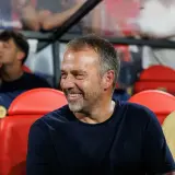 Uśmiechnięty mężczyzna, jeden z trenerów Barcelony, siedzi na ławce rezerwowych obok innych członków sztabu.