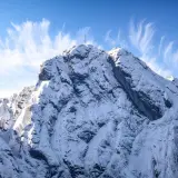 Ośnieżony szczyt Giewontu z krzyżem, pod błękitnym niebem z pierzastymi chmurami. Zastanawiasz się, ile trwa wejście na Giewont?