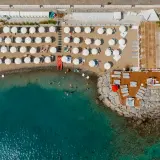 Vue aérienne d'une plage de Diano Marina avec des parasols blancs, des chaises longues, des baigneurs dans la mer turquoise et un jacuzzi sur la jetée.