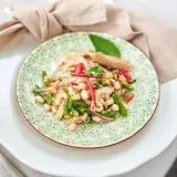 Ein bunter Thunfisch-Bohnen-Salat, italienisch inspiriert, mit grünen Bohnen, roten Zwiebeln und Tomaten auf einem Teller mit grünem Muster.