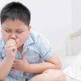 Un niño con pijama a cuadros tose con fuerza, agarrándose el pecho. Mi hijo no para de toser, parece que necesita ayuda.