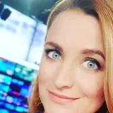Dagmara Kaczmarek Szalkow z TVN Fakty z błękitnymi oczami i blond włosami, w tle ekrany.