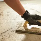 Arbeiter verlegt Estrich mit Glättkelle. Der frische Estrich wird sorgfältig bearbeitet, um eine ebene Fläche zu schaffen.
