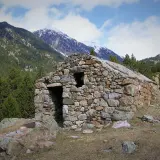 Antigua cabaña de piedra en el Vall de la Llosa, rodeada de pinos y montañas nevadas.