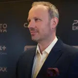Marcin Majewski z TVN w eleganckim garniturze, na tle logotypów PGE Ekstraklasa i Canal+.