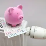 Różowa świnka-skarbonka na grzejniku z polskimi banknotami. Czy to symbol oszczędzania na rachunki, czy bon energetyczny dla każdego?