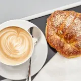 Cappuccino con latte art e brioche americane cosparse di zucchero.