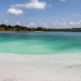 Lazurowe jezioro z piaszczystą plażą i lasem w tle. Woda jest krystalicznie czysta, a dno widoczne.