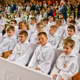 Dzieci w bieli na komunii świętej. Czy rocznica komunii jest obowiązkowa? Rodzice i goście obserwują uroczystość.