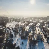 Zimowy krajobraz Krakowa z blokami mieszkalnymi i parkiem. Widać dymiące kominy w oddali, co może wpływać na ceny mieszkań w Krakowie.