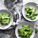 Drei Teller mit Rigatoni in cremiger, grüner veganer Spinatsoße, bestreut mit veganem Parmesan. Ein Genuss für Augen und Gaumen!