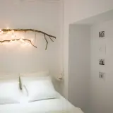 Ideas para decorar ramas secas: una rama con luces cálidas sobre la cama, fotos y mariposas en la pared.