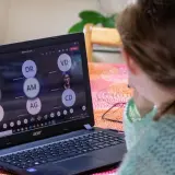 Dziewczynka uczestniczy w lekcji online przez msteams. Na ekranie laptopa widać wiele okręgów z inicjałami uczestników.
