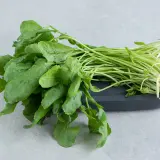 Un manojo fresco de el berro, con sus hojas verdes vibrantes y tallos delgados, descansa sobre una tabla oscura.
