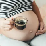 Kobieta w ciąży trzyma filiżankę kawy. Delikatny napój dla przyszłych mam.