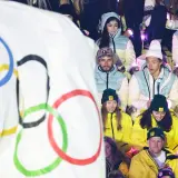 Młodzi sportowcy w barwach narodowych, z flagą olimpijską w tle, czekają na start reprezentacji Polski na Zimowe Igrzyska Olimpijskie 2026.