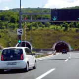 Biały samochód zbliża się do tunelu w Chorwacji. Znak drogowy informuje o opłatach za autostrady.