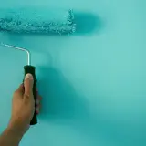 Mano sujetando un rodillo de pintura turquesa, ideal para conseguir el mejor rodillo para pintar paredes lisas.
