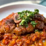 Herzhaftes Ossobuco mit einer reichhaltigen Tomaten-Gemüse-Sauce und frischer Kräuter-Gremolata als Beilage.