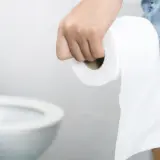 Dłoń trzymająca rolkę papieru toaletowego, w tle sedes. Stres wywołuje biegunka.