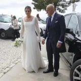 Novia con ramo de lirios y su acompañante, un hombre con traje de raya diplomática, llegan a su boda. Irene Matamoros, radiante.