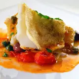 Delicioso bacalao encebollado con tomates, aceitunas y alcaparras en una salsa naranja vibrante.