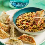 A gyoza is dipped into a flavorful gyoza dipping sauce with scallions and chili flakes.