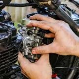 Manos ajustando el ahogador de moto, pieza clave para el arranque en frío.