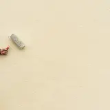 Mano con rullo per pittura facciata esterna, su scala, che rinnova il muro di colore giallo chiaro.