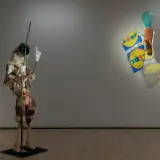 Konsthallar Sverige: En surrealistisk figur med päls och en pinne står bredvid en väggskulptur med Lidl-påsar och ett grönt huvud.