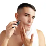 Mężczyzna goli twarz golarką elektryczną na białym tle.