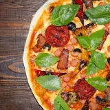 Pyszna california pizza z kiełbaskami, bekonem, pieczarkami i świeżą bazylią na drewnianym blacie.