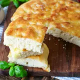 Frisch gebackene Focaccia, ein köstliches original focaccia rezept, mit Tomaten, Oliven und Basilikum auf einem Holzbrett.