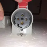 Zbliżenie na gniazdo do podłączenia wtyczki siłowej. Widoczne styki i mechanizm zabezpieczający.