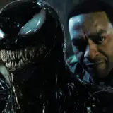 Venom, le symbiote noir aux dents acérées, se rapproche d'un homme au regard intense. Une scène prometteuse pour Venom 3.